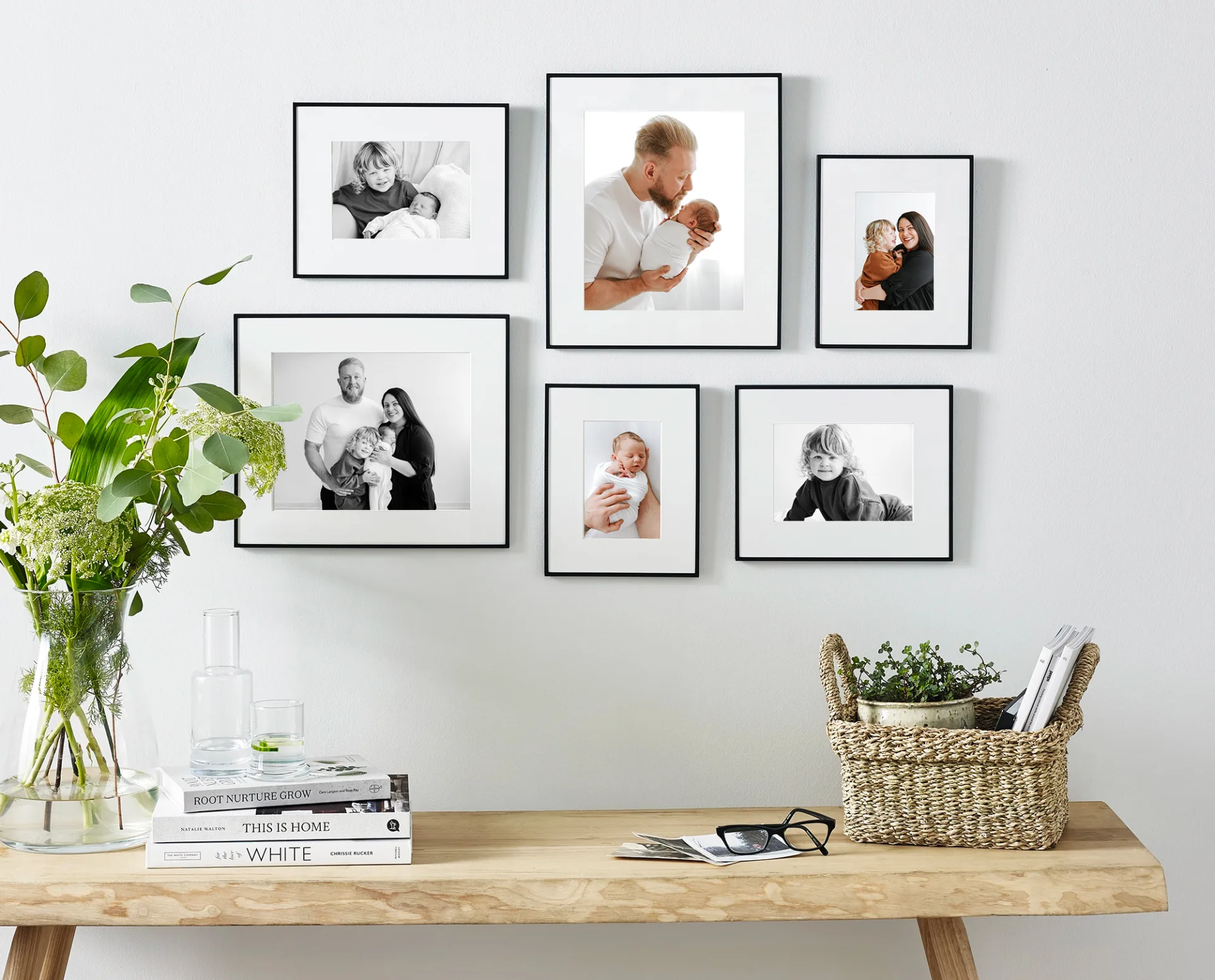 photo of an entryway with photo frames on the wall. There's also a plant in a glass jar and a basket, both on a wooden bench