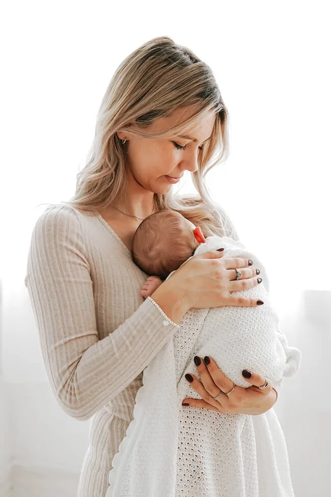 professional photo of a newborn baby wrapped in a blanket being held by a young woman in a glasgow portrait studio