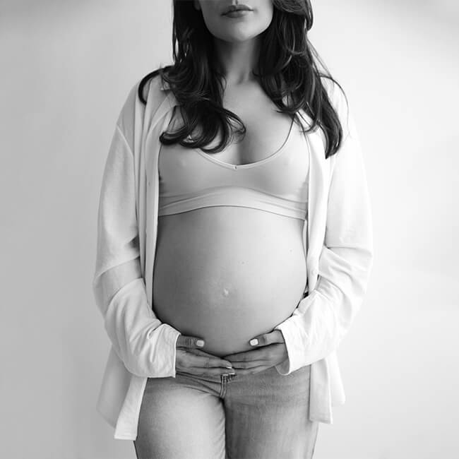 A black and white shot of the pregnant woman from the waist up, softly lit.