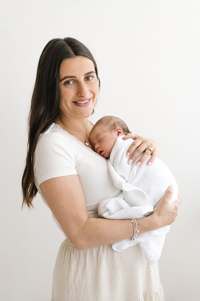 A mother holding her newborn close to her chest, smiling warmly at the camera.